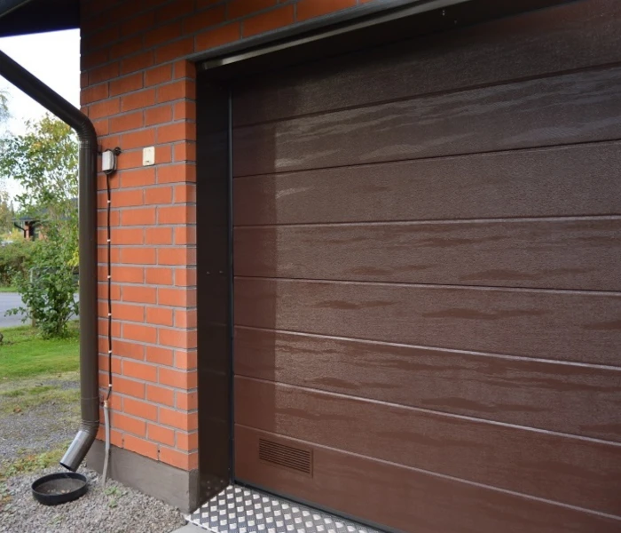 Autotallin nosto-ovi Kouvolassa asennettuna peltipielellä — leveä vaakaura puunsyy — JK-Ovet