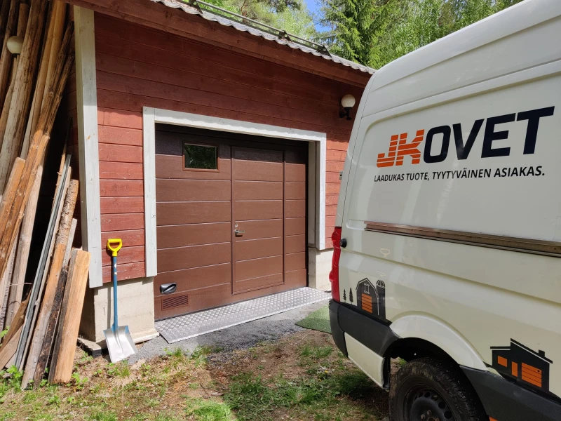 Autotallin ovi ikkunalla ja käyntiovella Pertunmaalla — turkkipeltikynnys — leveä vaakaura — JK-Ovet